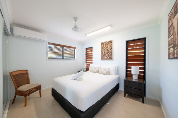 A bedroom with a bed, a chair, a nightstand, a wall-mounted air conditioner, and a ceiling fan.