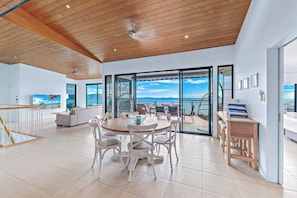 A spacious living area with a round wooden table, white chairs, a sofa, and a balcony with a view.