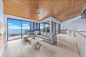 A modern living room with a large sofa, a coffee table, and a view of the sea.
