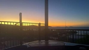 A sunset view from a balcony with a railing and a distant bridge.
