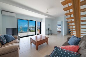 A spacious living room with a wooden coffee table, two sofas with patterned cushions, a TV, and a balcony with a view.