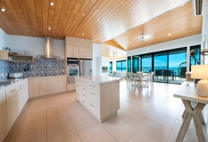 A modern kitchen with wooden ceiling, large windows, and a dining area with a view.