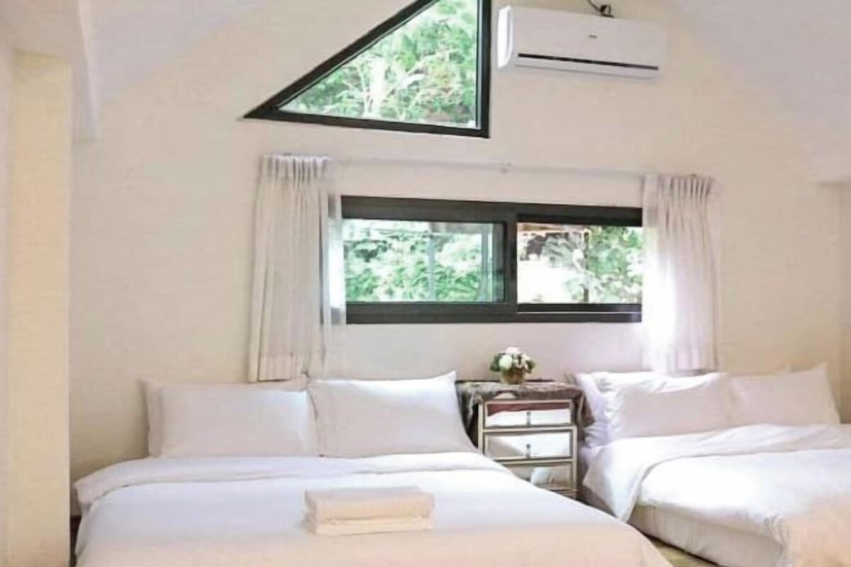 Un dormitorio con dos camas, una ventana con cortinas, un equipo de aire acondicionado y una mesita de noche con lámpara.
