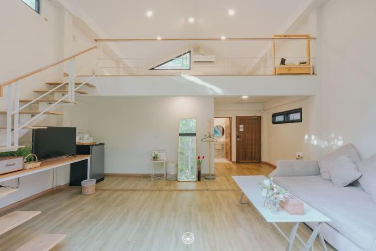 Un salón espacioso con una escalera que lleva a un nivel superior, un televisor de pantalla plana, un sofá y una mesa de centro.
