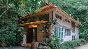 A rustic house with a wooden porch, surrounded by lush greenery and potted plants. - My Cottage Chiangmai (Mae On)