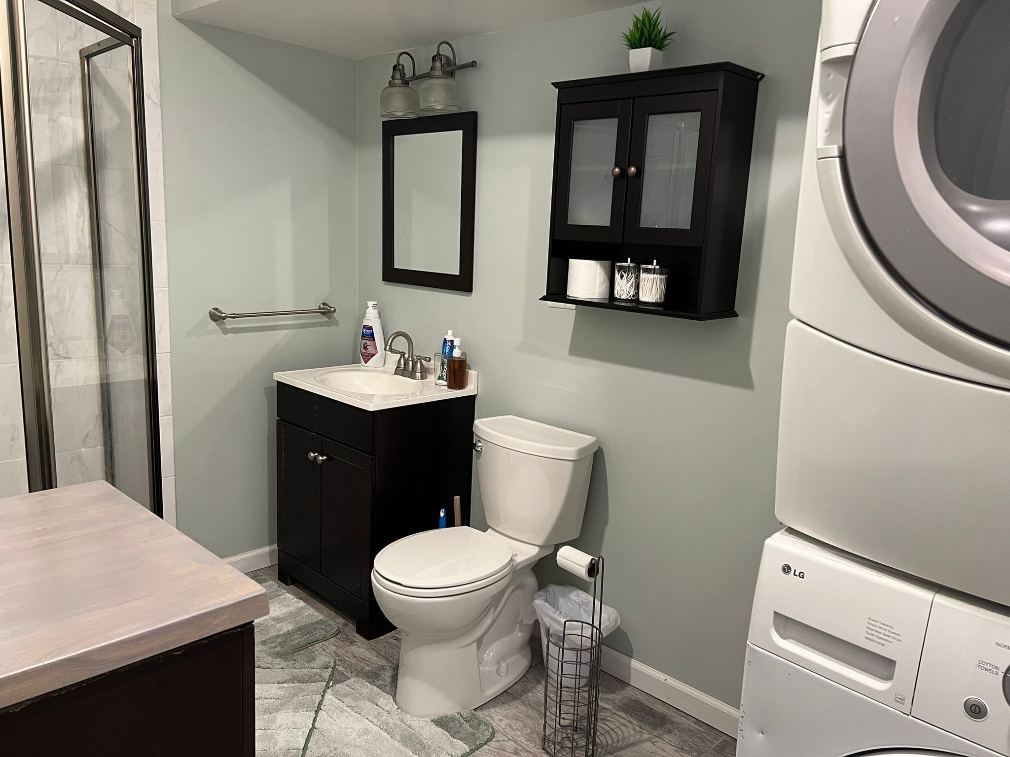 A bathroom with a toilet, sink, cabinet, mirror, and a washing machine.