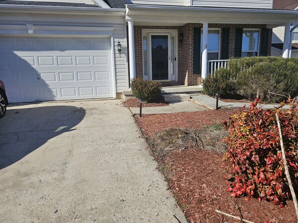 A residential house with a garage, a front porch, and a small garden area with mulch and shrubs.
