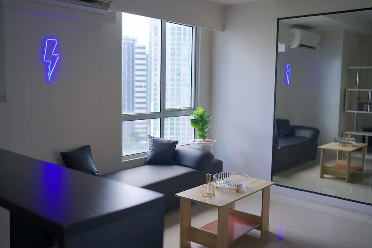 A modern living room with a sofa, a small table, and a large window offering a city view.