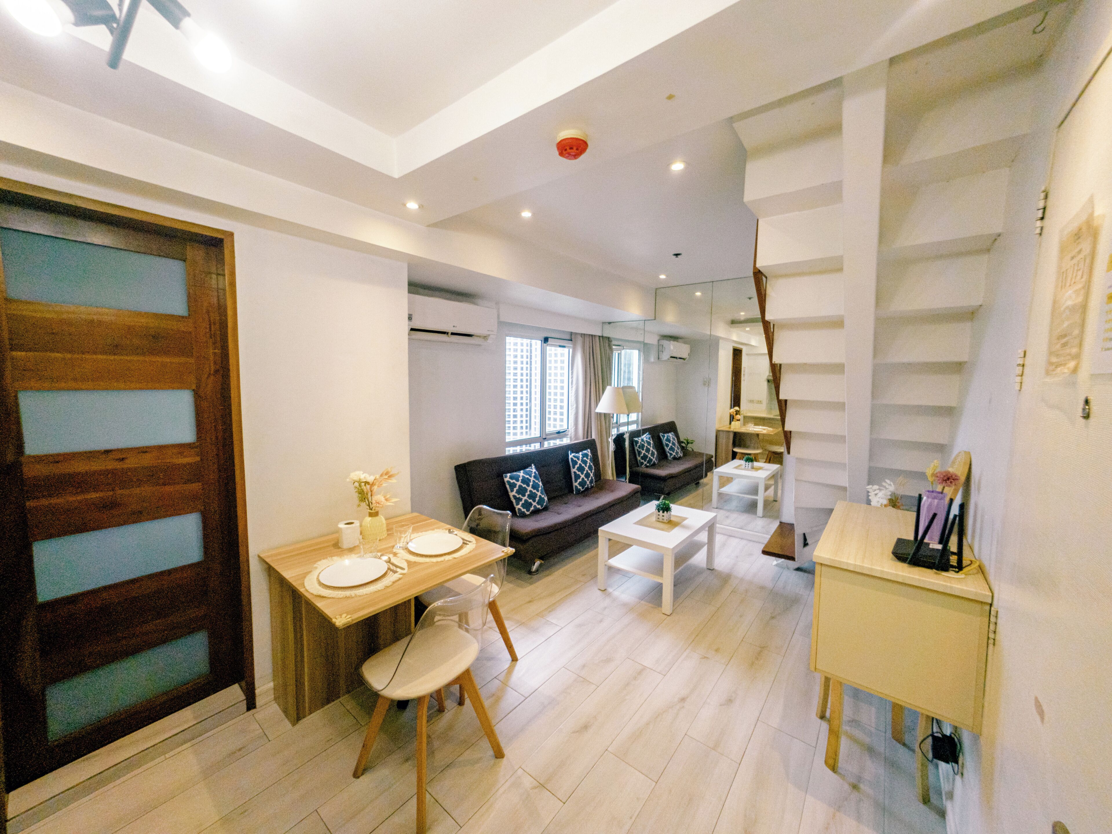 A modern living room with a dining area, a sofa set, and a staircase.