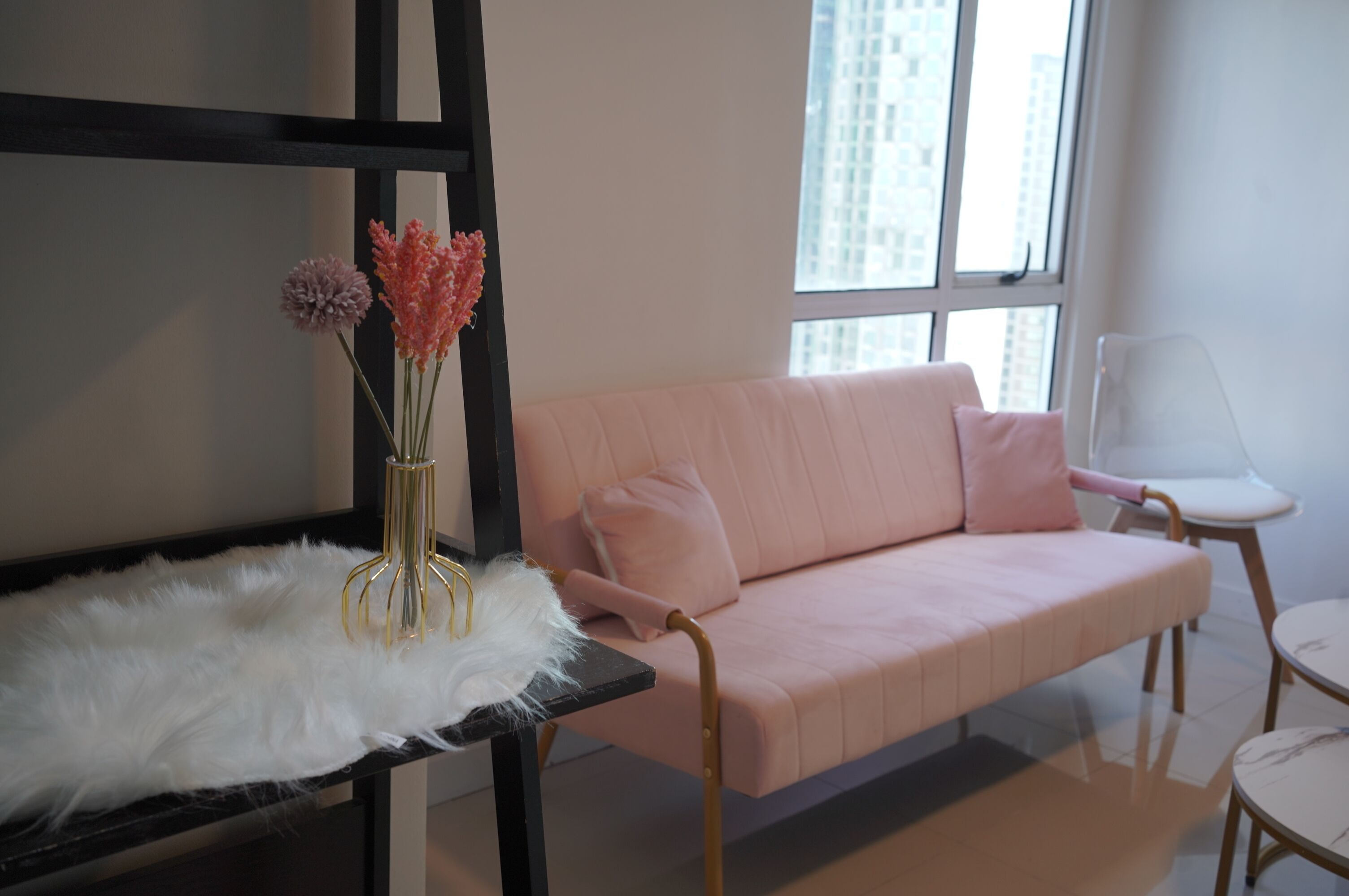 A modern living room with a pink sofa, a white fluffy rug, and a vase with flowers.
