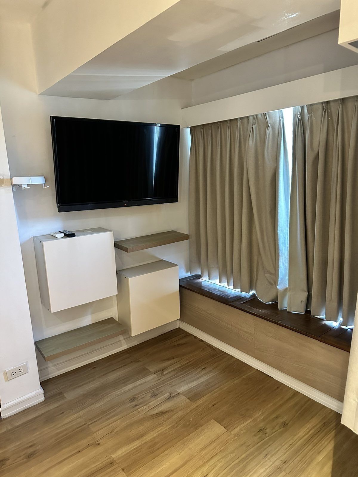 Una sala de estar moderna con un televisor de pantalla plana montado en la pared, un banco empotrado con espacio de almacenamiento y un gran ventanal con cortinas.