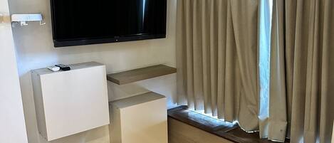 Una sala de estar moderna con un televisor de pantalla plana montado en la pared, un banco empotrado con espacio de almacenamiento y un gran ventanal con cortinas.