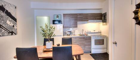 A compact kitchen with modern appliances, a dining area with a table and chairs, and a potted plant.