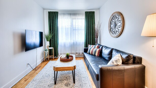 A modern living room with a leather sofa, a flat-screen TV, a coffee table, and a decorative wall piece.