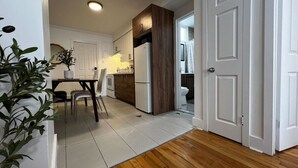 A modern kitchen with white cabinets, a wooden accent wall, and a dining area with a table and chairs. - Stylish 1 Bedroom in Saint-Laurent (Montréal)