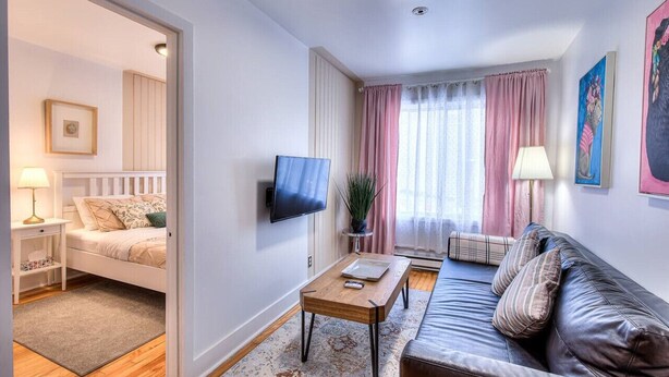 A modern living room with a bed, a sofa, a TV, and a window with curtains. - Stylish 1 Bedroom in Saint-Laurent (Montréal)