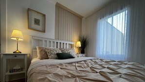 A bedroom with a large bed, two bedside tables, a nightstand, a framed picture, and sheer curtains. - Stylish 1 Bedroom in Saint-Laurent (Montréal)