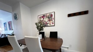 A dining area with a wooden table, white chairs, a vase with flowers, and a wall-mounted picture. - Stylish 1 Bedroom in Saint-Laurent (Montréal)