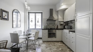 A modern kitchen with white cabinets, a gas stove, an oven, and a microwave. There is a dining table with chairs and a window with a view of the city.