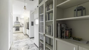 A hallway with a marble floor, a kitchen area with white cabinets, and a bookshelf filled with books and a lantern.
