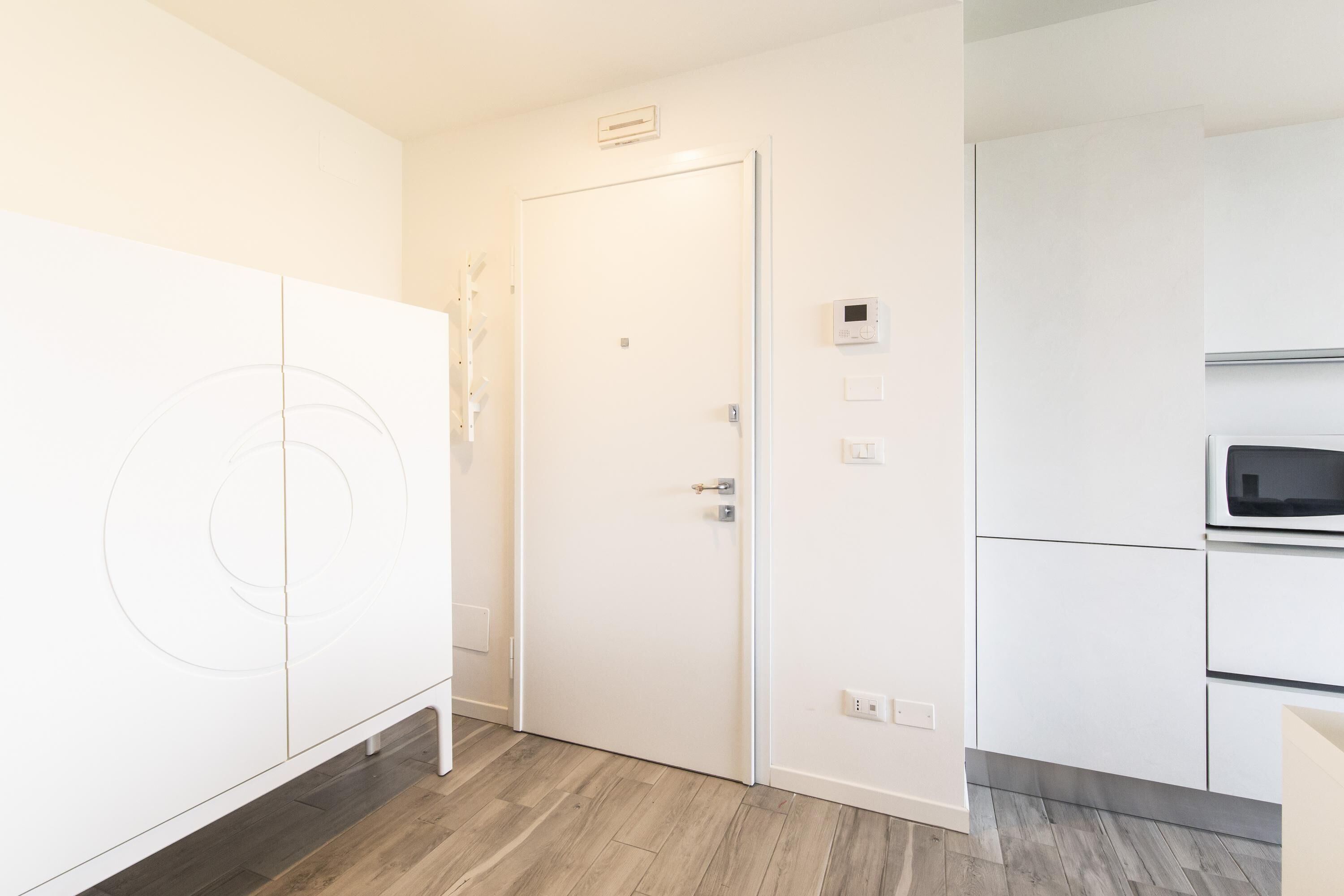 A modern kitchen with white cabinetry, a microwave, and a door with a handle.