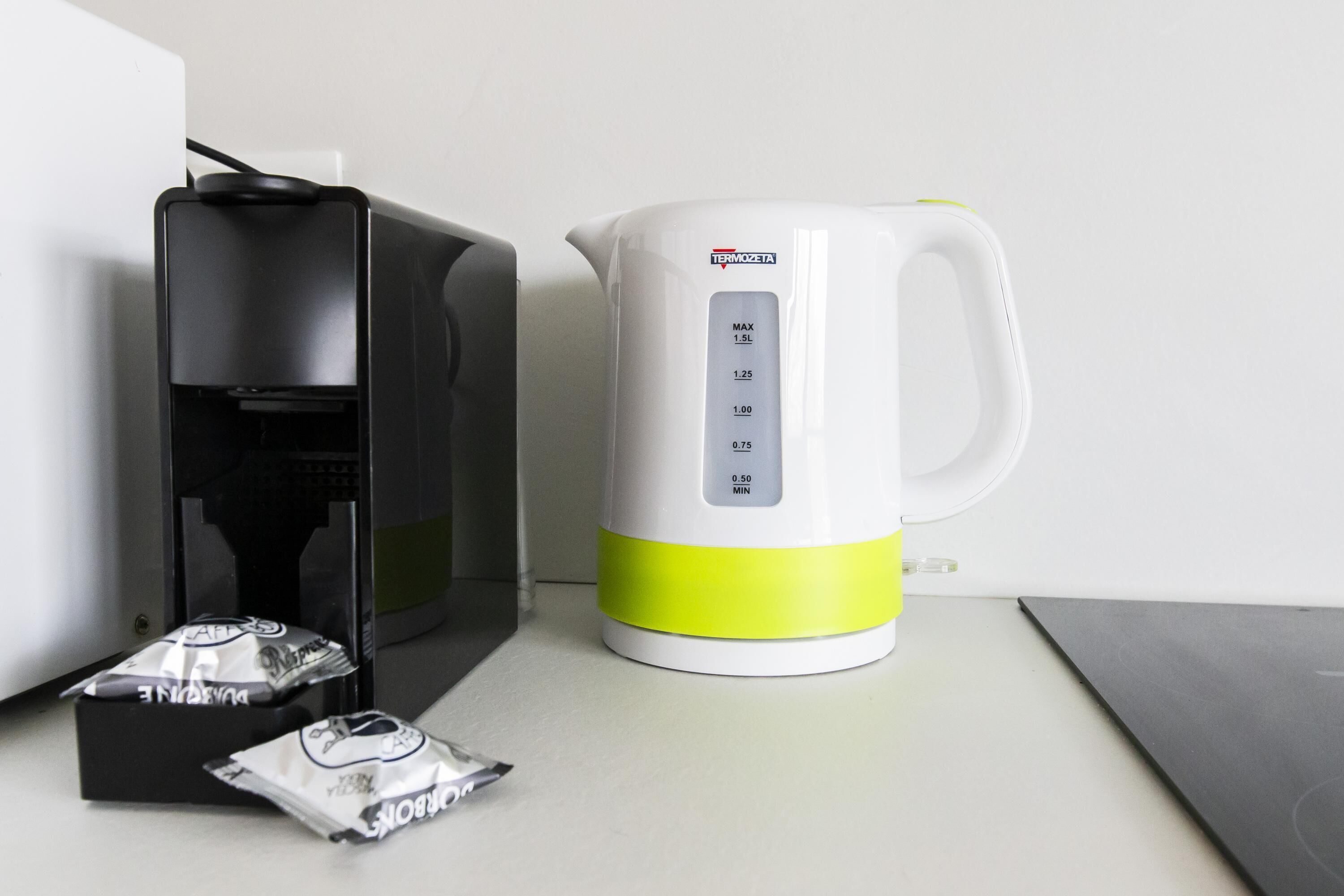 A coffee maker, a kettle, and two packets of coffee on a countertop.