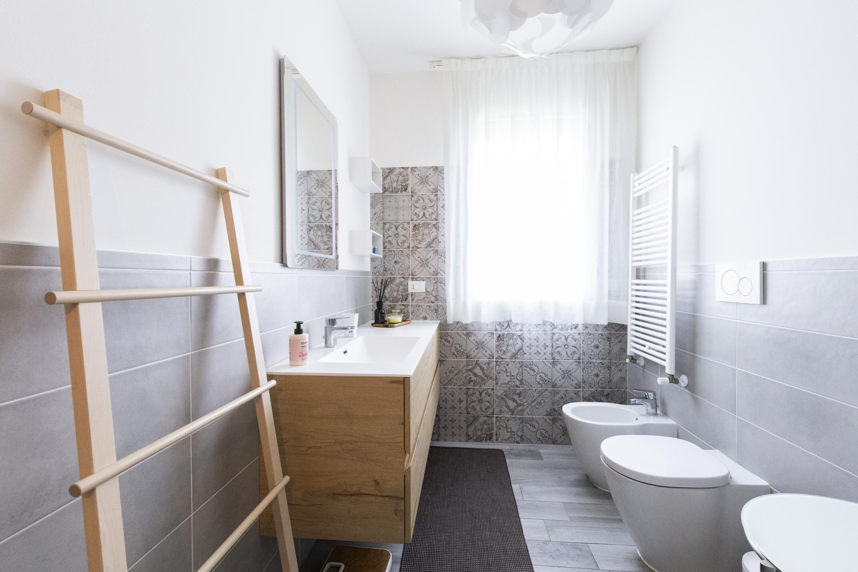 A modern bathroom with a wooden vanity, a towel rack, a mirror, a toilet, and a bidet.