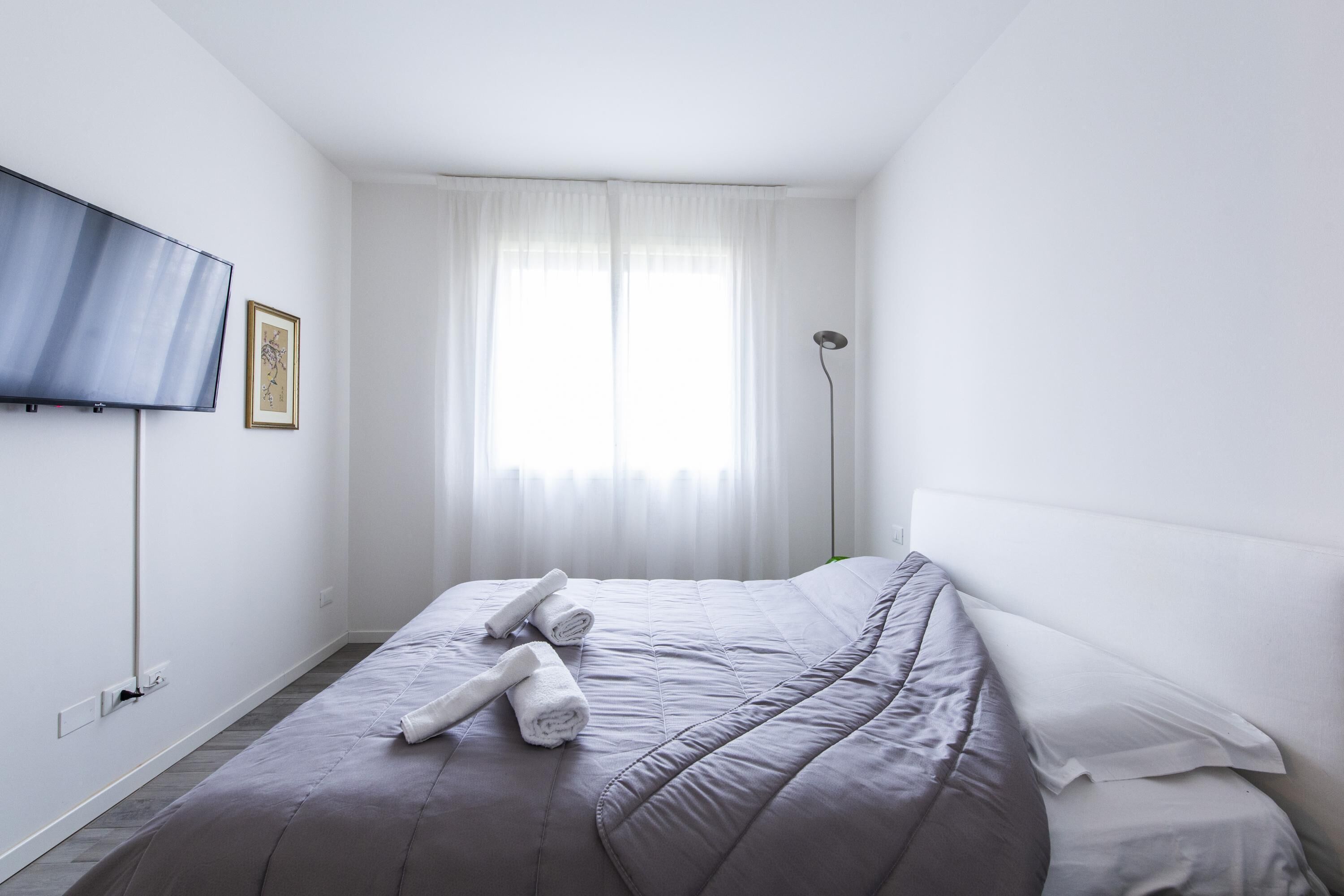 A bedroom with a bed, a TV mounted on the wall, and a window with curtains.