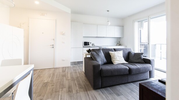 Un salon moderne avec un canapé gris, une petite table et un coin cuisine à l’arrière-plan.