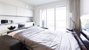 Une chambre d’hôtel moderne dotée d’un grand lit, d’un bureau, d’une kitchenette et offrant une vue sur l’extérieur.