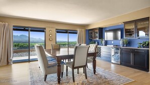 A modern kitchen with a large dining table, dark cabinets, and a view of mountains through large windows. - The Tubac Alegria Retreat (Tubac)