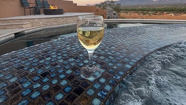 A glass of white wine on a mosaic-tiled table by a hot tub with a view of mountains. - The Tubac Alegria Retreat (Tubac)