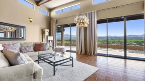A spacious living room with a large sofa, a glass coffee table, and a view of mountains through large windows. - The Tubac Alegria Retreat (Tubac)
