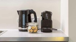 Een aanrecht met een waterkoker, een koffiezetapparaat en een potje theezakjes.