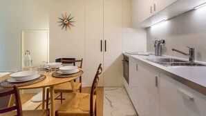 Een moderne keuken met witte kastjes, een roestvrijstalen spoelbak en een eethoek met een houten tafel en stoelen.