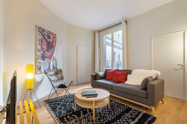 A living room with a sofa, a coffee table, a TV, a lamp, and a painting on the wall.