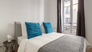 Une chambre à coucher avec un lit, une table de chevet avec une lampe et une fenêtre avec des rideaux.