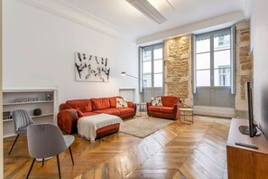 Ein modernes Wohnzimmer mit Fischgrätparkett, einer roten Sofagarnitur, einem grauen Sessel und einer Wand mit Steinverkleidung.