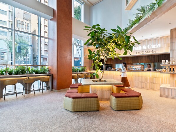 Un café moderno con un amplio ventanal, plantas de interior y una zona central con taburetes acolchados.