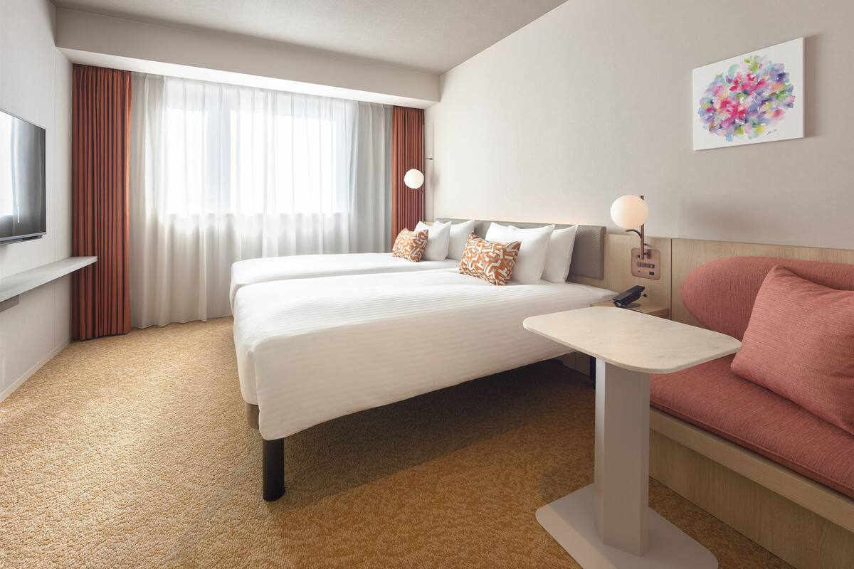 A hotel room with a large bed, a small table, a sofa, a TV, and a painting on the wall.