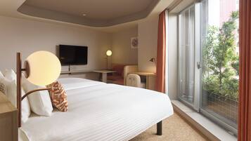 A hotel room with a large bed, a desk, a chair, a television, and a balcony with a view of greenery.