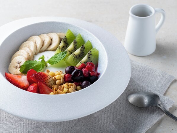 Un tazón de ensalada de frutas con plátanos, kiwi, fresas y arándanos sobre un plato blanco.