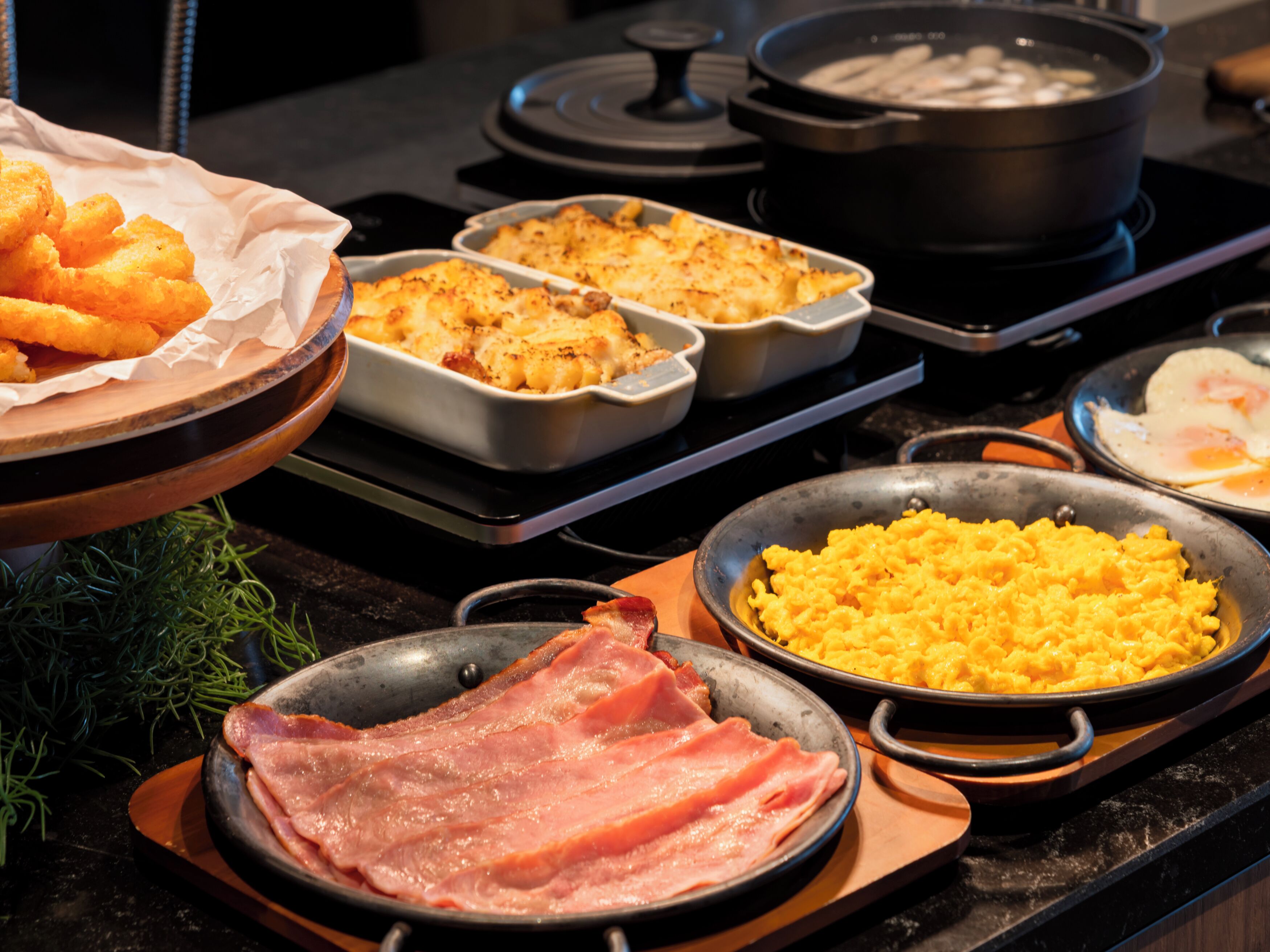 Un bufé con diversos platos, incluyendo huevos revueltos, macarrones y jamón.