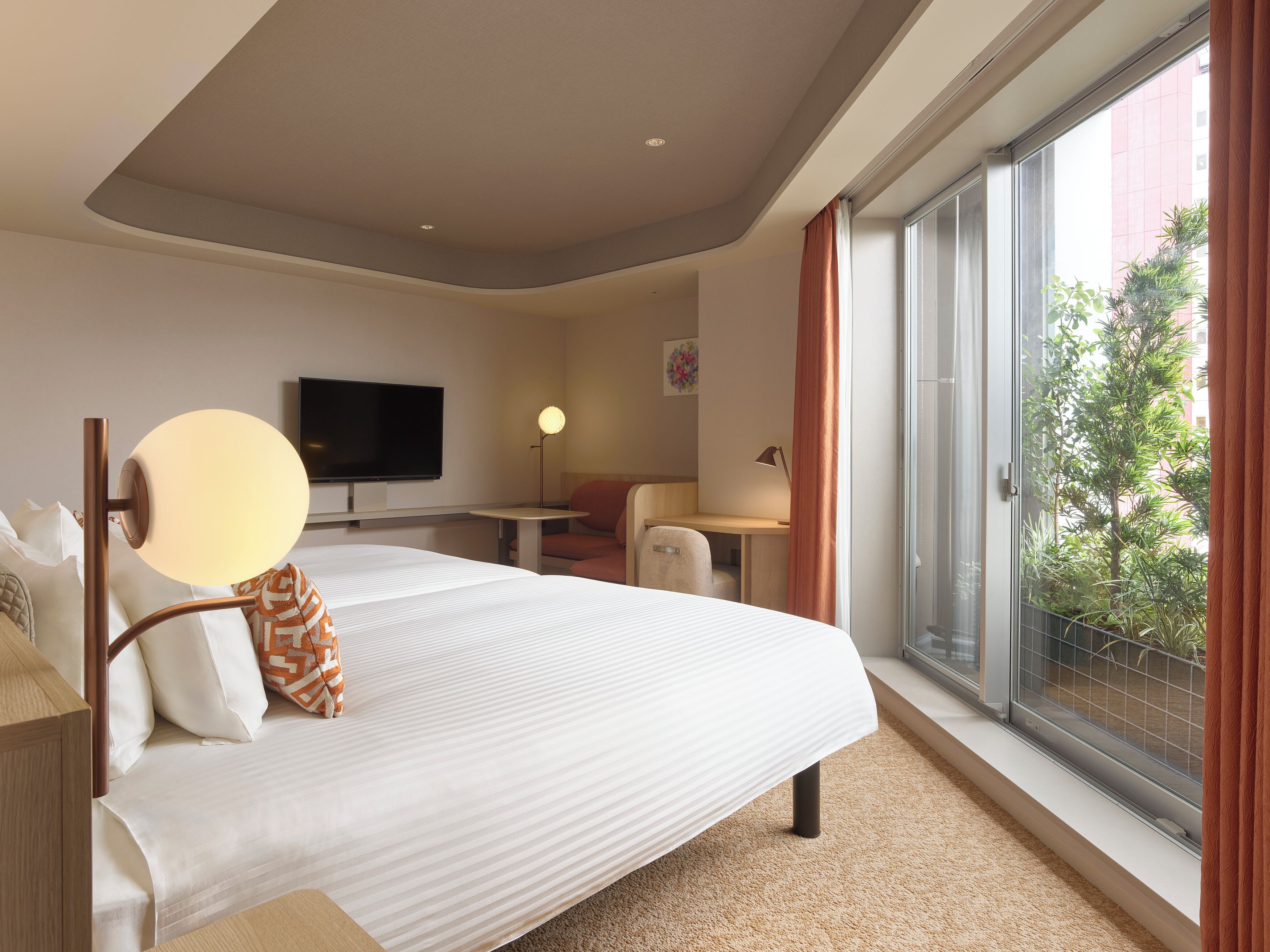 A hotel room with a bed, a desk, a chair, a television, and a large window with a view of greenery.