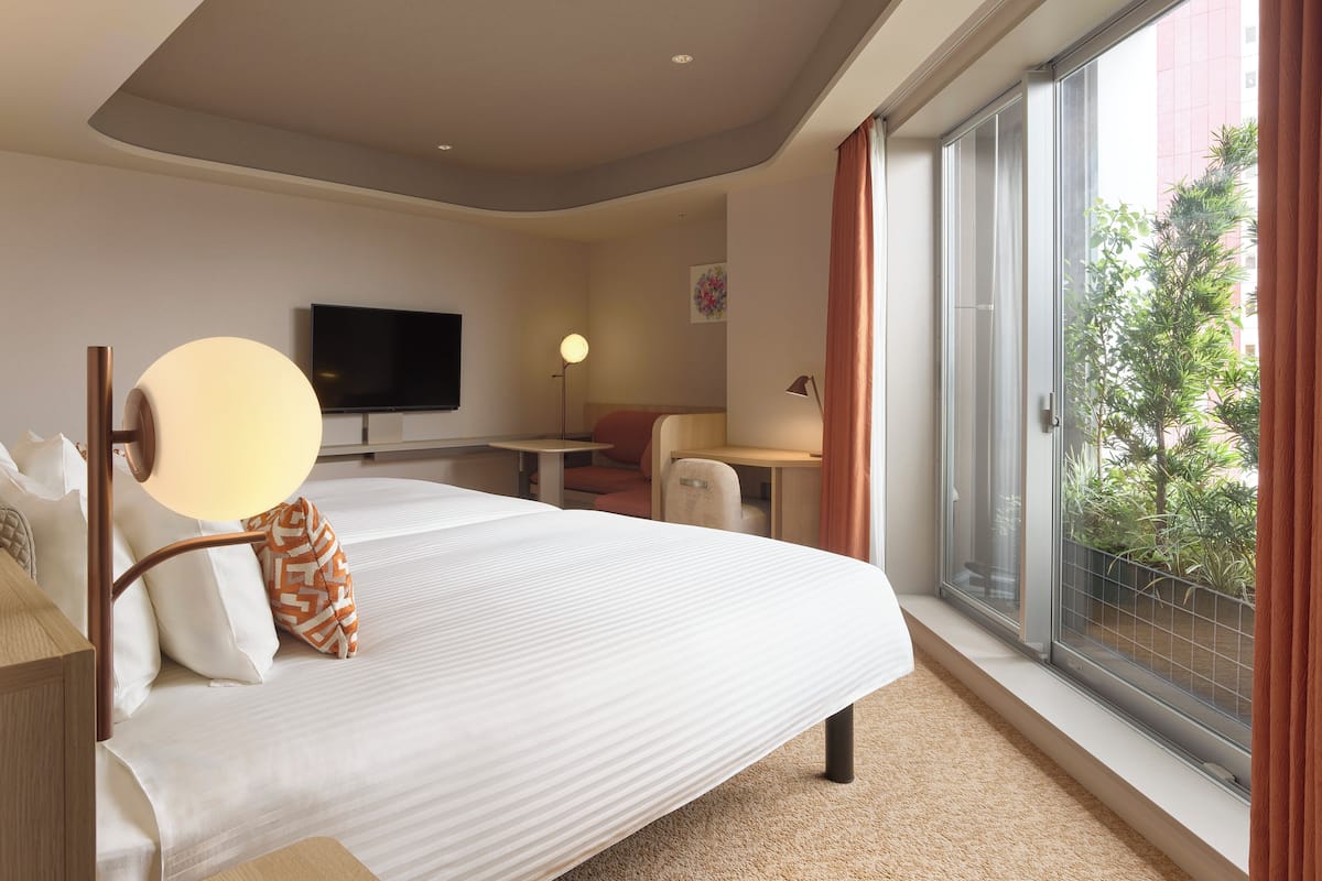 Habitación de hotel con una cama grande, un escritorio, una silla, un televisor y un balcón con vistas a zonas verdes.