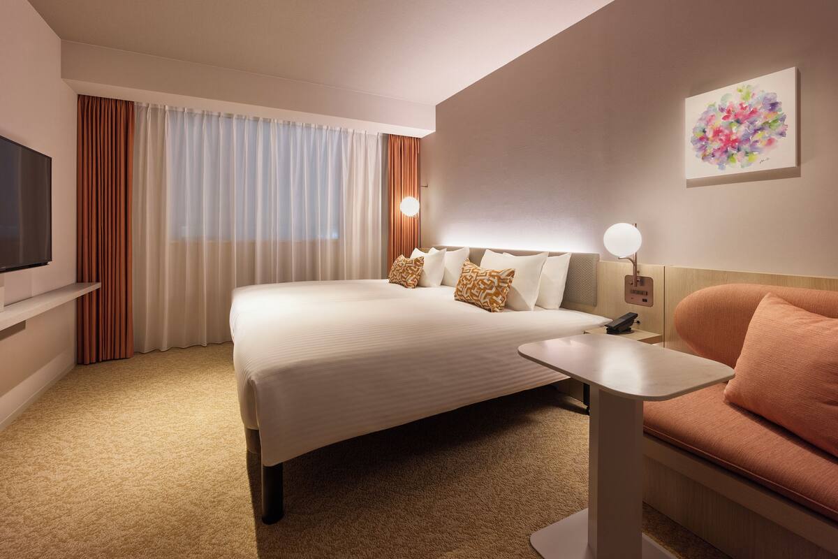 A hotel room with a large bed, a bedside table, a TV, and a painting on the wall.