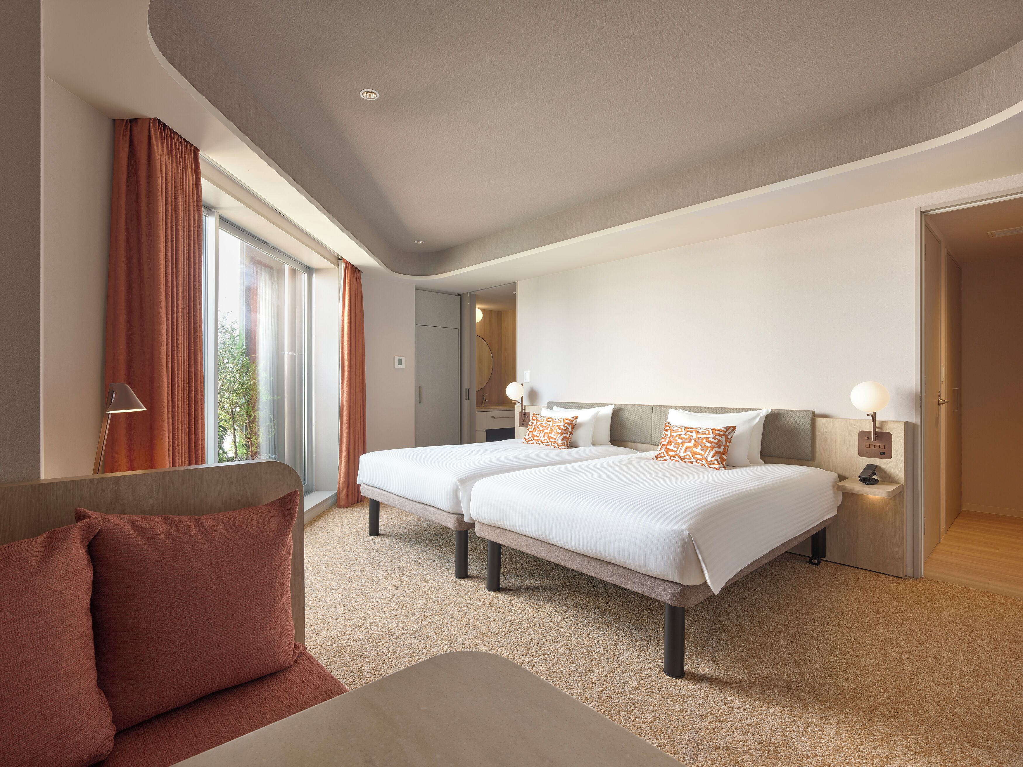 Une chambre d’hôtel moderne avec deux lits, un canapé et une grande fenêtre avec des rideaux.