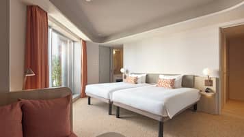 Une chambre d’hôtel moderne avec deux lits, un canapé et une grande fenêtre avec des rideaux.