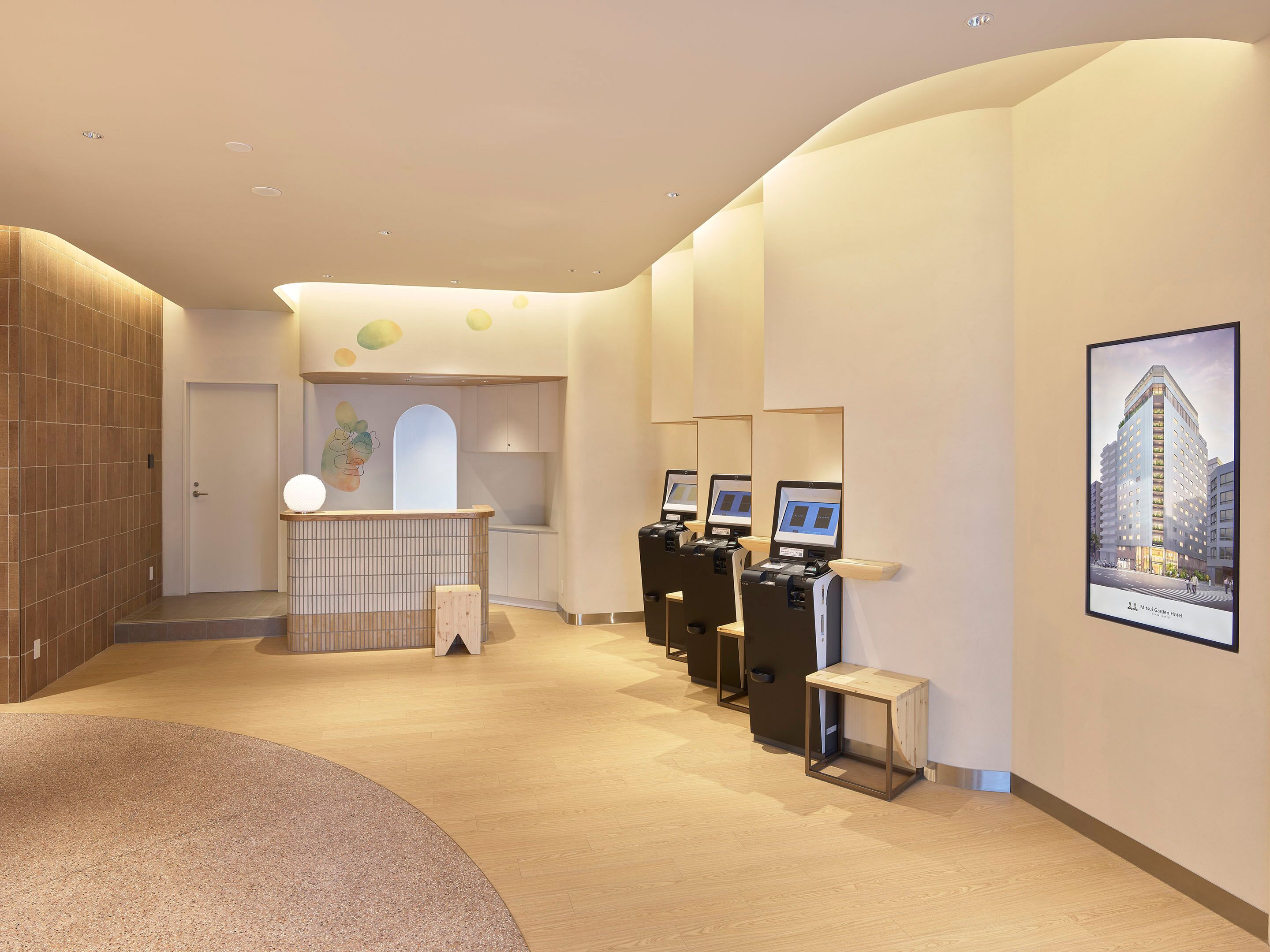 A modern hotel lobby with a reception desk, seating area, and a large poster of the hotel building.