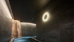 A modern indoor swimming pool with dark stone walls and a circular light fixture. - Mitsui Garden Hotel Ginza Tsukiji (Tokyo)